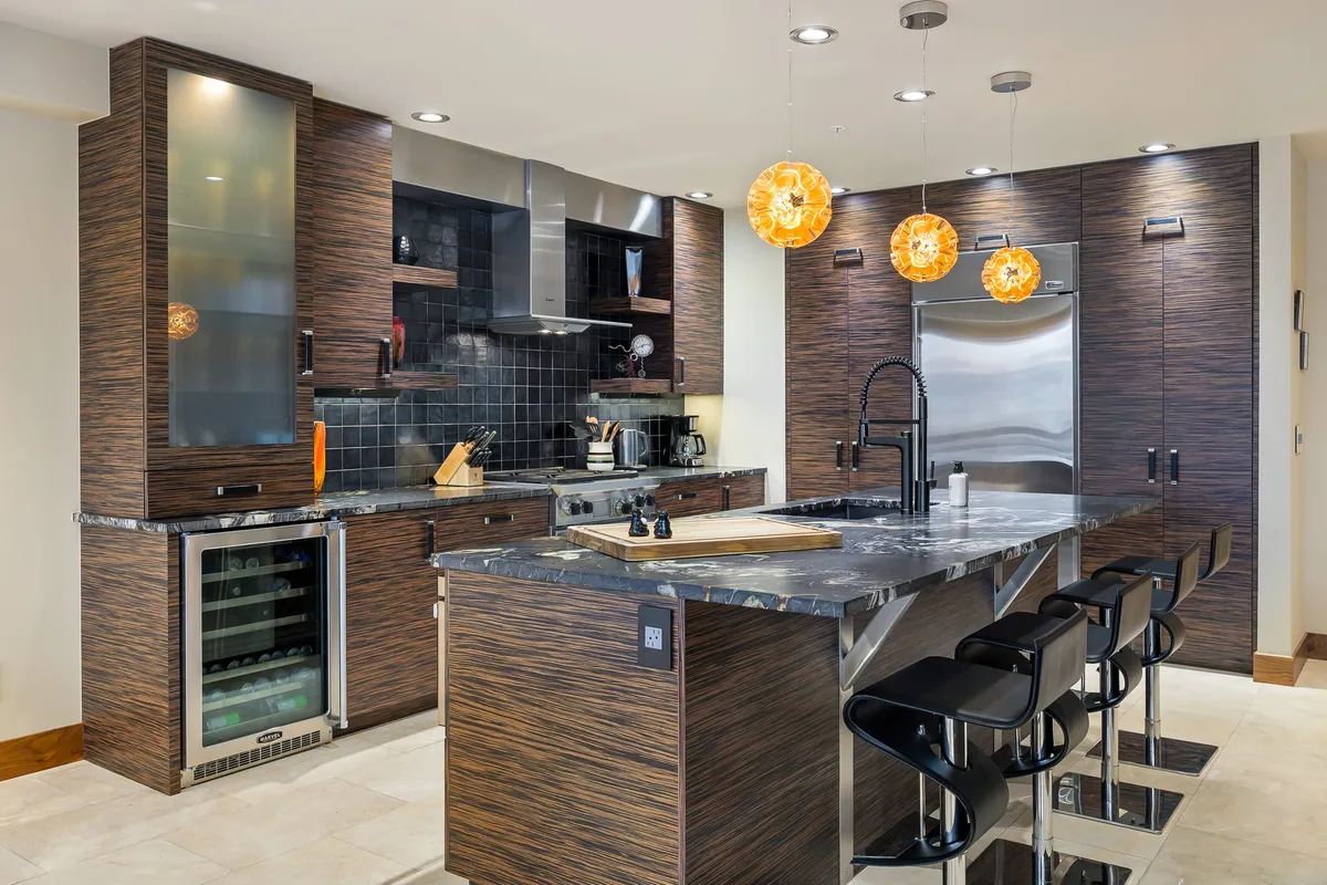 This image features a modern kitchen with a spacious island countertop, stylish pendant lighting, a sleek black backsplash, and high-end kitchen appliances. The setting is perfect for both cooking and entertaining, with an ambiance that balances sophistication and warmth.