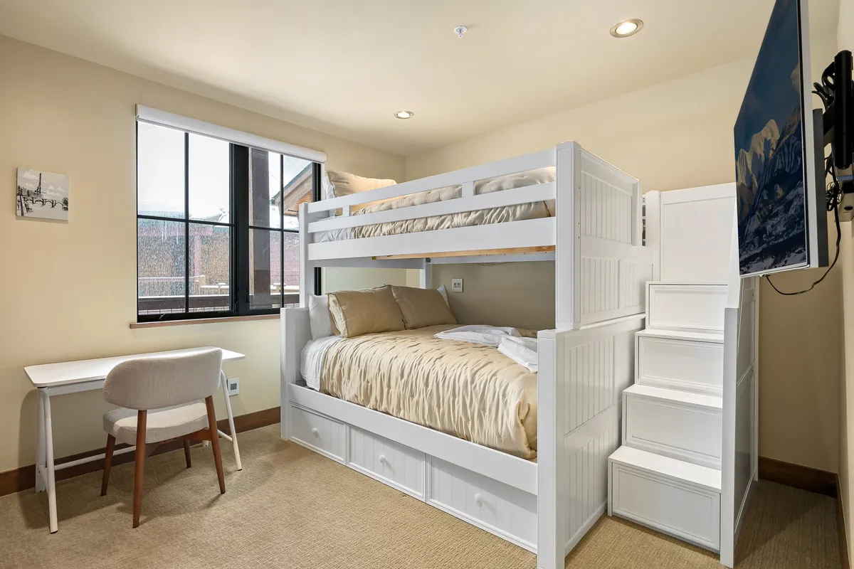 A cozy bunk bedroom with a sturdy XL full-over-queen bunk bed, a window that brings in daylight, and an adjacent desk area for studying or play. The room has a relaxed, kid-friendly vibe, perfect for group or family retreats.