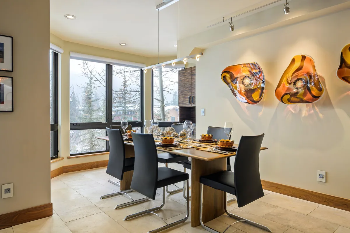 A spacious dining area highlighted by a large table, vibrant wall art, and oversized windows that bathe the room in natural light. The setup is designed for family meals, dinner parties, and casual get-togethers, emphasizing shared experiences.