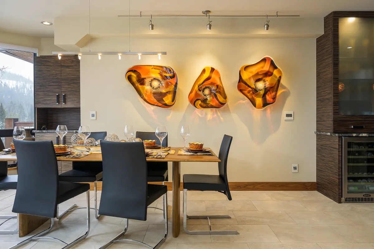 A tastefully set dining table is surrounded by modern chairs and enhanced by artistic wall decor. The space exudes warmth and sophistication, ideal for gatherings and special meals shared with friends or loved ones.