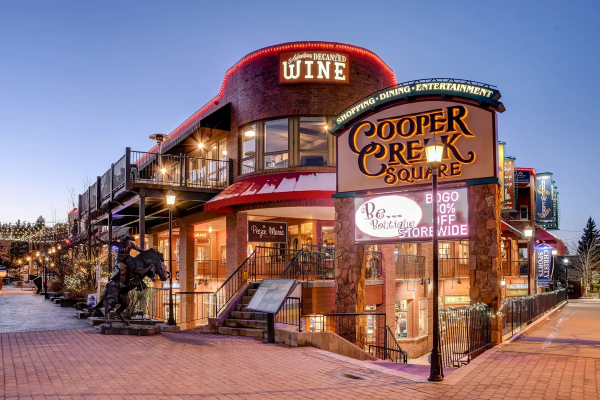 The inviting entrance to Cooper Creek Square, featuring a wine shop, outdoor seating, decorative lighting, and a festive atmosphere. The setting is lively yet intimate, suggesting opportunities for wine tastings, dining, and social gatherings close to the retreat.
