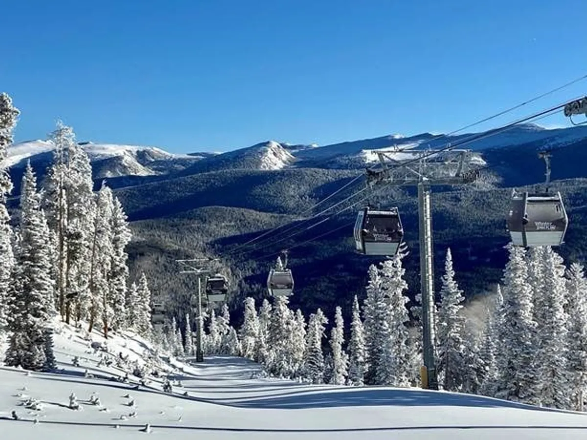 An exhilarating winter scene featuring a gondola lift gliding above snow-covered trees with a dramatic mountain range in the background. The crisp snow and bright sky evoke the thrill of adventure, while the gondola suggests easy access to skiing, snowboarding, and scenic rides.